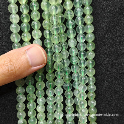 Close up view of Grade A clean prehnite round beads on hand showing light transmission and clean matrix