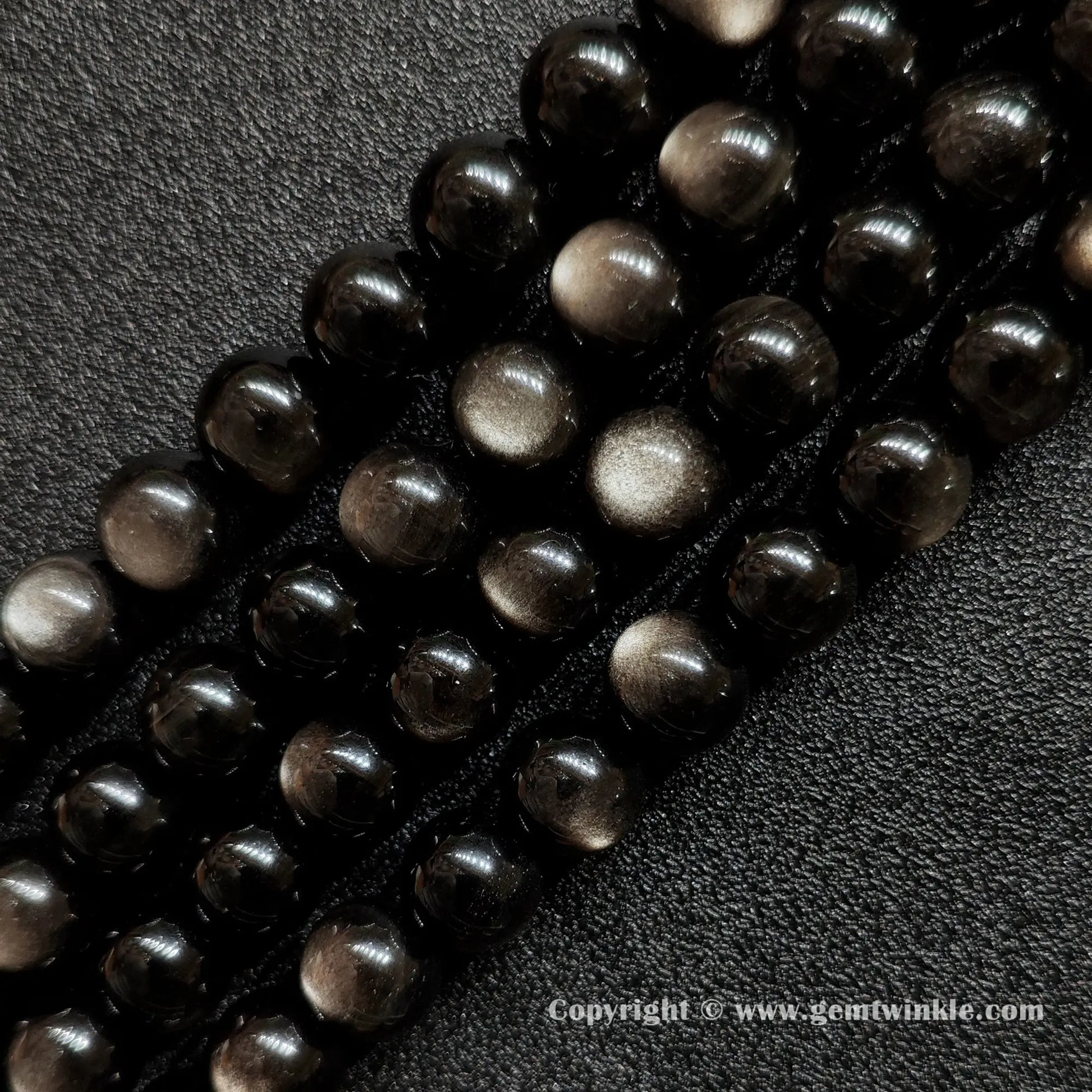 Angled view of Grade A silver sheen obsidian gemstone strands highlighting smooth polish and silver reflections