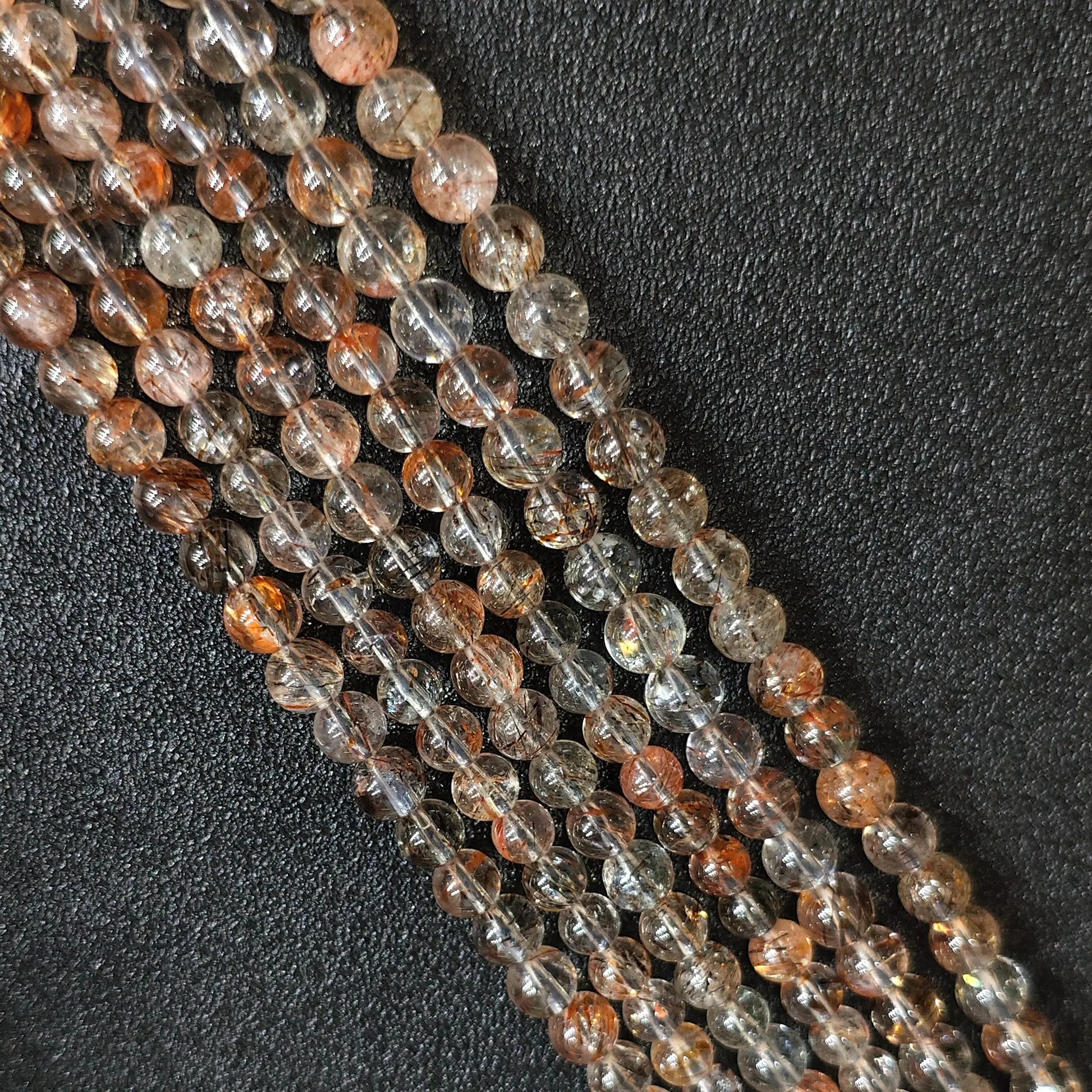 Macro closeup of Grade B black gold super seven quartz smooth round beads showing natural copper and golden inclusions