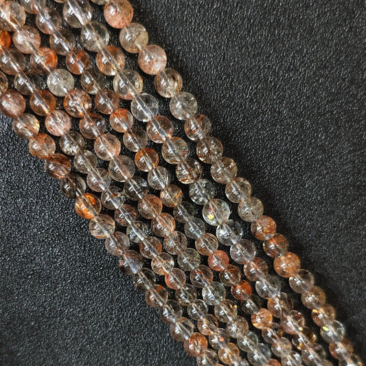 Macro closeup of Grade B black gold super seven quartz smooth round beads showing natural copper and golden inclusions