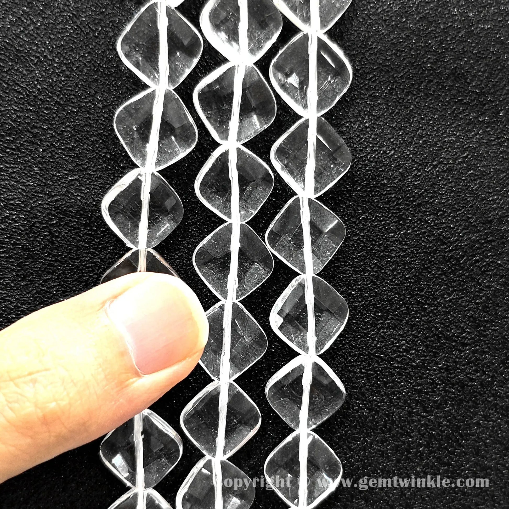 Hand holding 14mm natural clear quartz faceted diamond flat beads strand