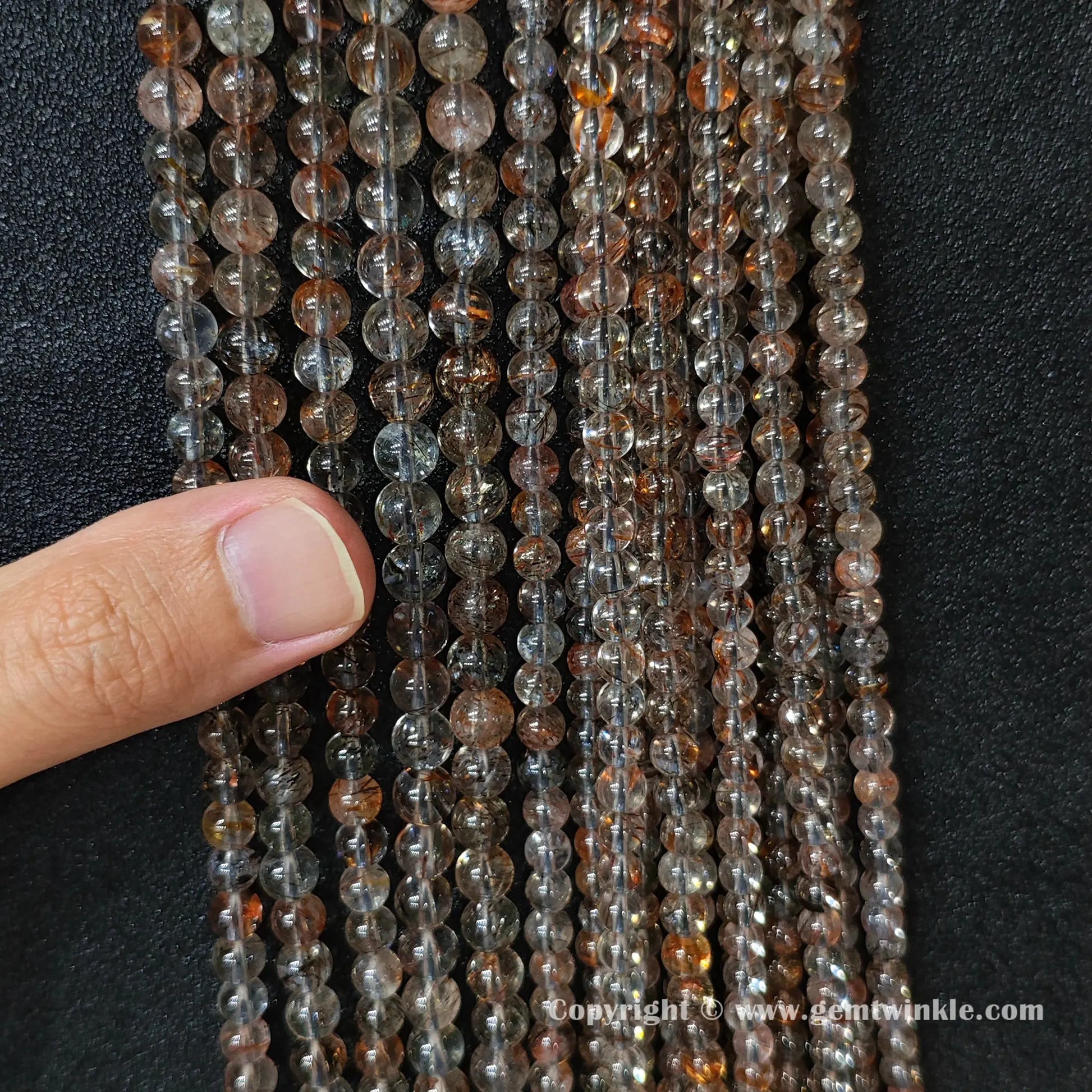 Close up view of Grade B black gold super seven round beads held on hand for natural inclusion distribution preview
