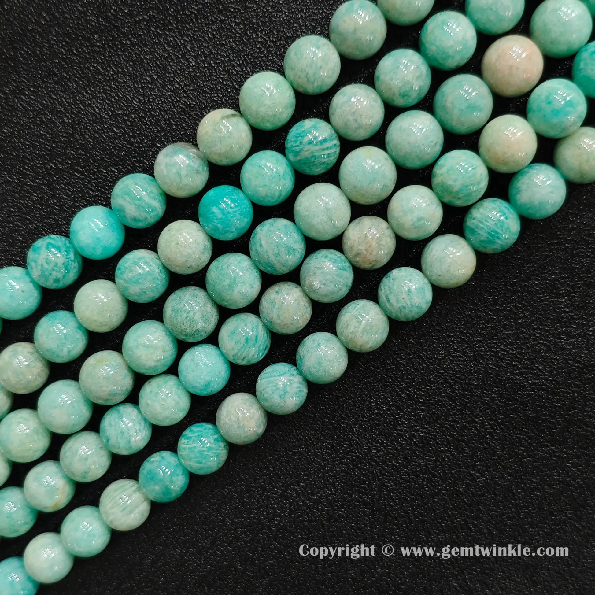Multiple strands of Grade C natural amazonite round beads with earthy yellow matrix on dark background