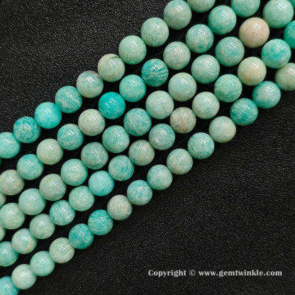 Multiple strands of Grade C natural amazonite round beads with earthy yellow matrix on dark background