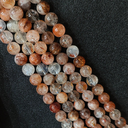 Macro closeup of Grade C black gold super seven quartz smooth round beads showing copper red and dark inclusions