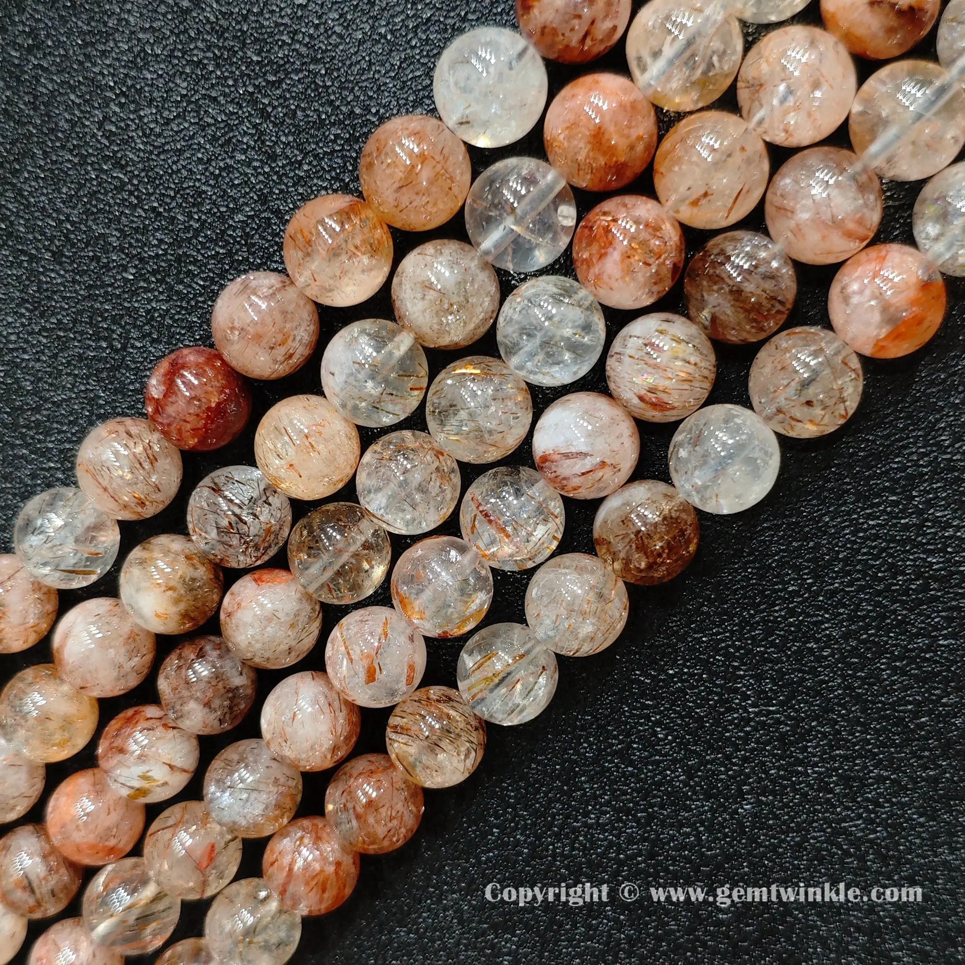 Angled view of Grade C black gold super seven round bead strands laid parallel on dark surface
