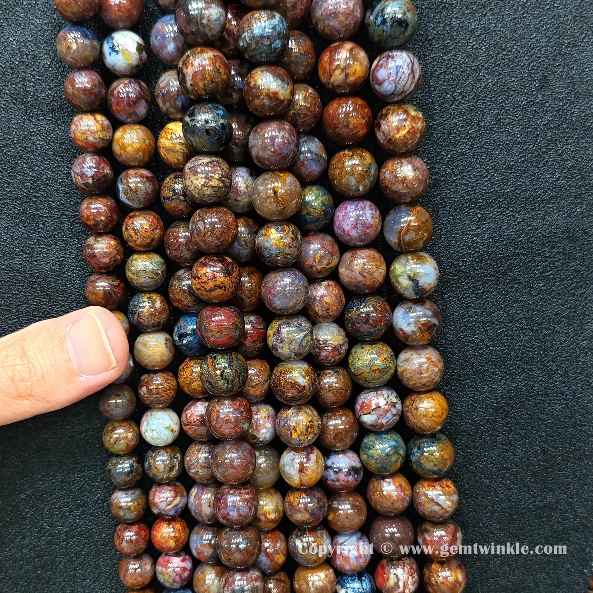 Close up view of Grade C pietersite round beads held on hand for natural color variation preview