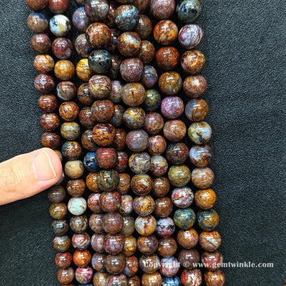 Close up view of Grade C pietersite round beads held on hand for natural color variation preview