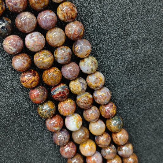 Macro closeup of Grade C pietersite smooth round beads showing earthy red and brown swirling breccia patterns