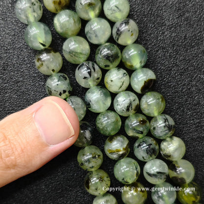 Close up view of Grade C prehnite round beads held on hand showing natural black inclusion distribution