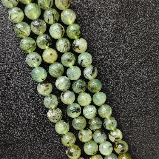 Macro closeup of Grade C prehnite smooth round beads showing green body with black tourmaline inclusions