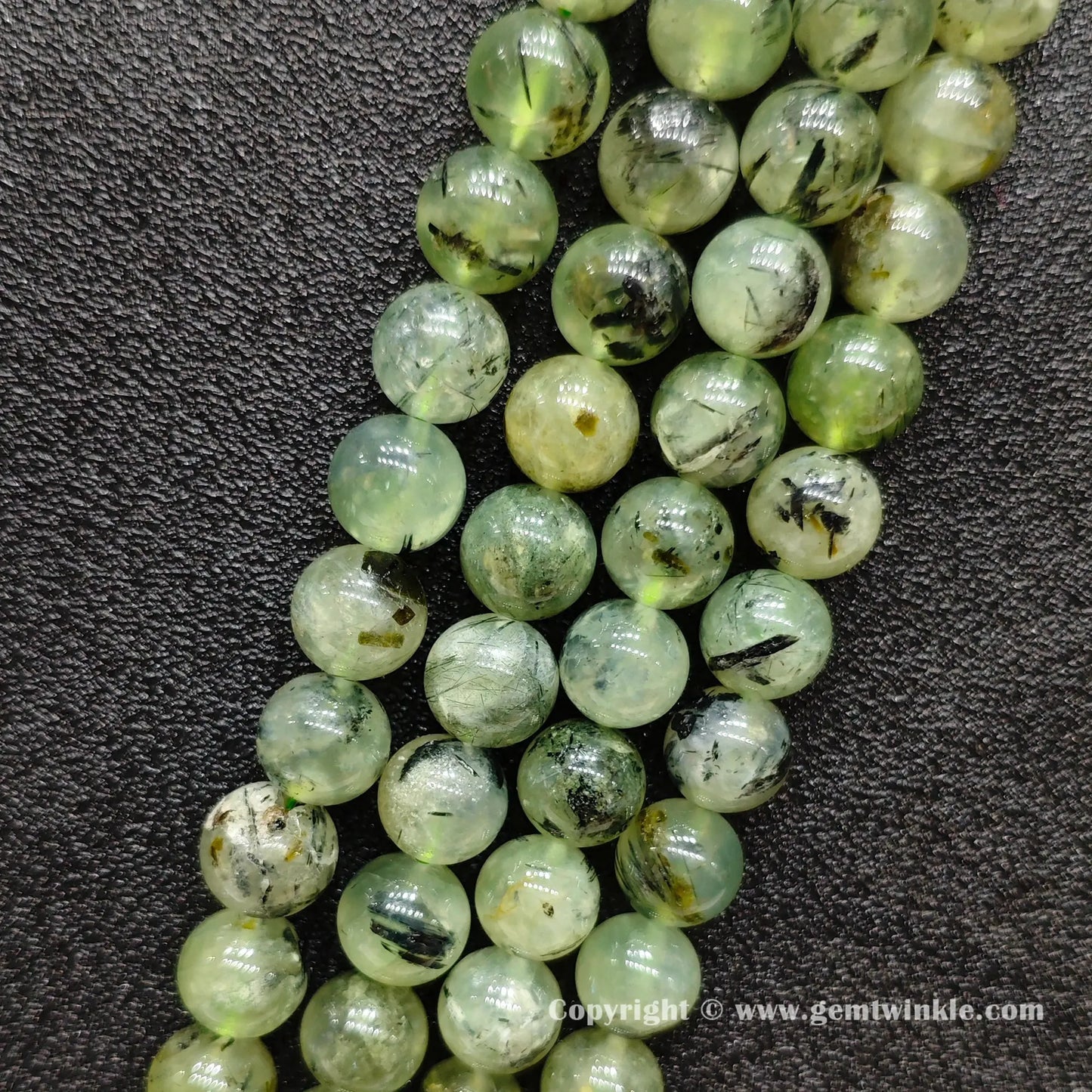 Angled view of Grade C prehnite round bead strands with black needle inclusions laid parallel