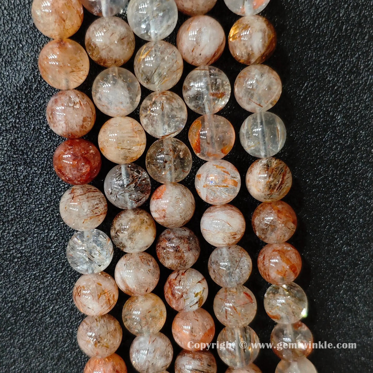 Perspective view of Grade C black gold super seven quartz round beads showing polished surface across 4mm to 12mm