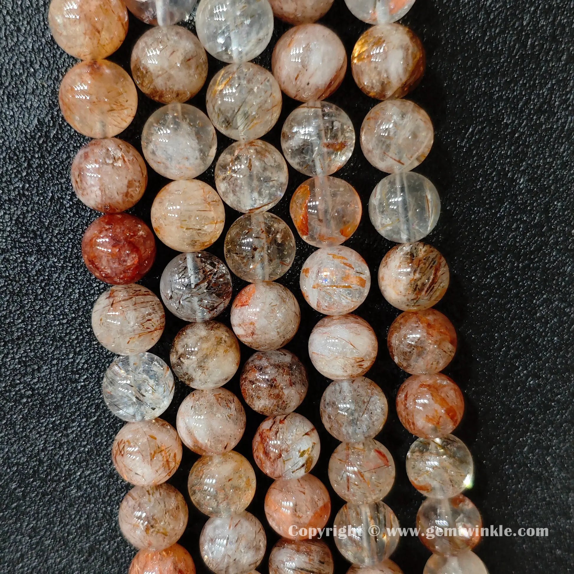 Perspective view of Grade C black gold super seven quartz round beads showing polished surface across 4mm to 12mm