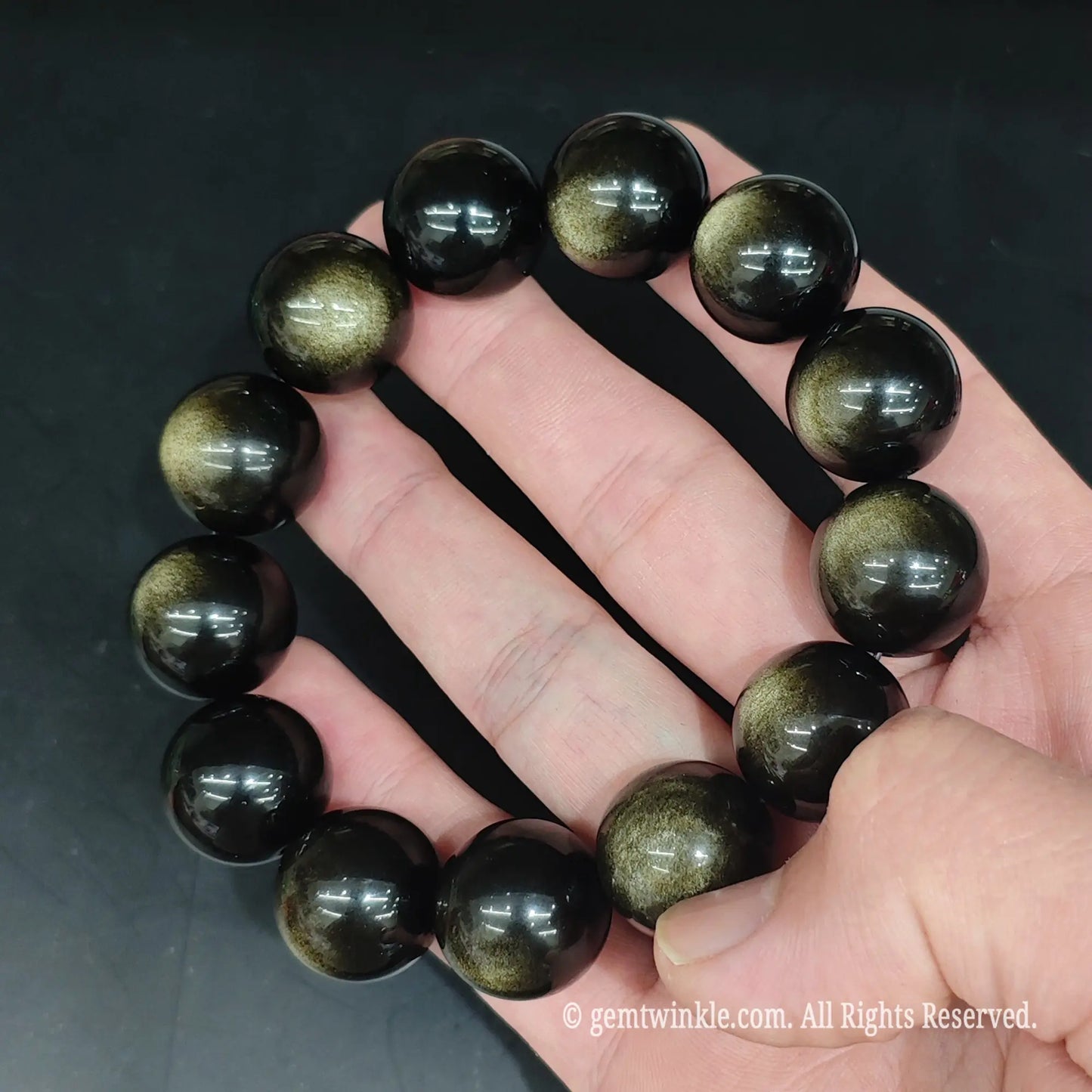 Full view of Grade A golden volcanic obsidian stretch bracelet resting open on hand showing smooth beads
