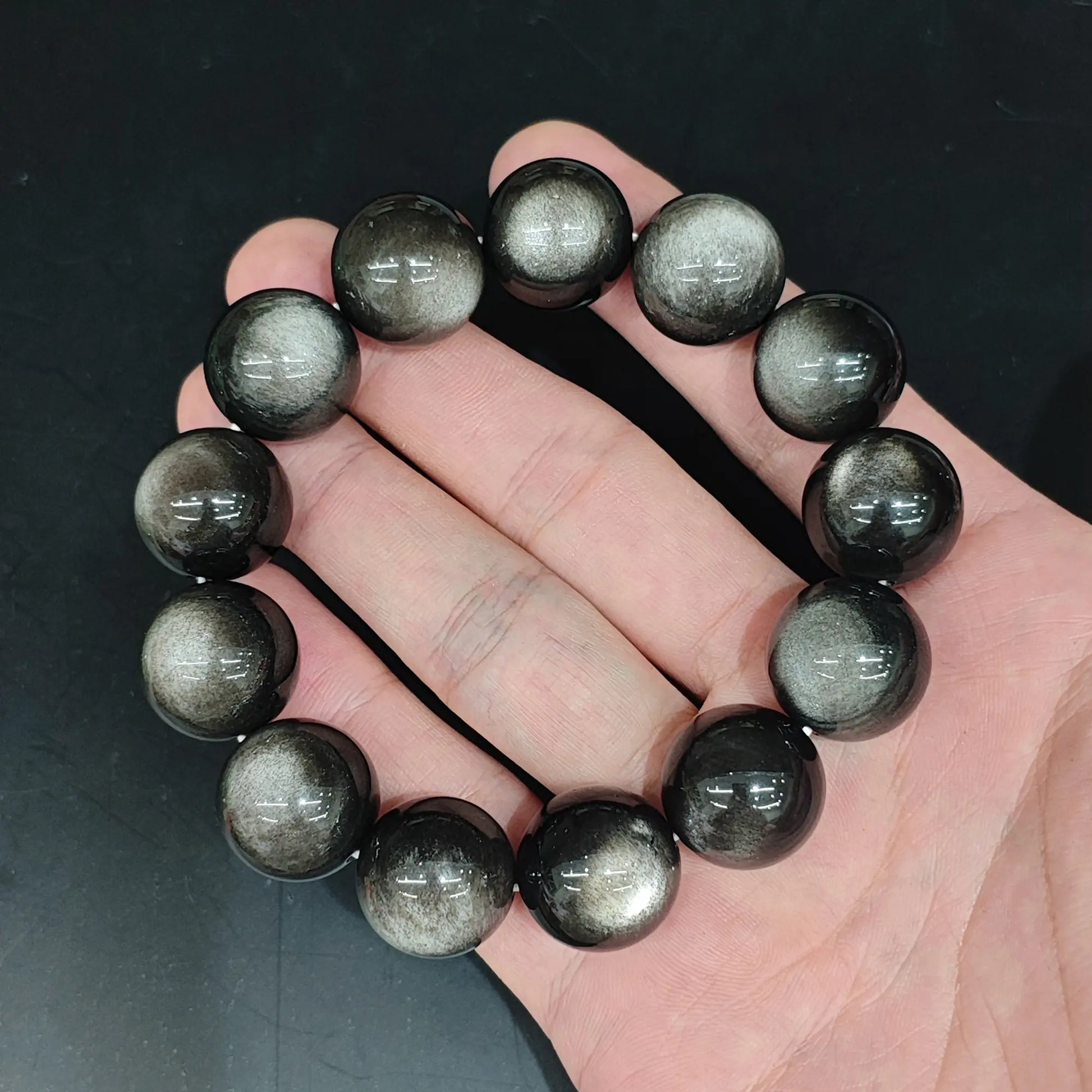 Grade A silver sheen obsidian cat's eye round bead bracelet held close up showing sharp silver eye line and glossy black finish