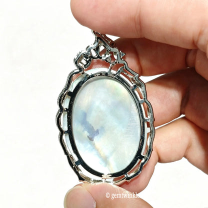 Back view of shell cameo pendant held up to light showing smooth iridescent mother of pearl surface and bezel backing