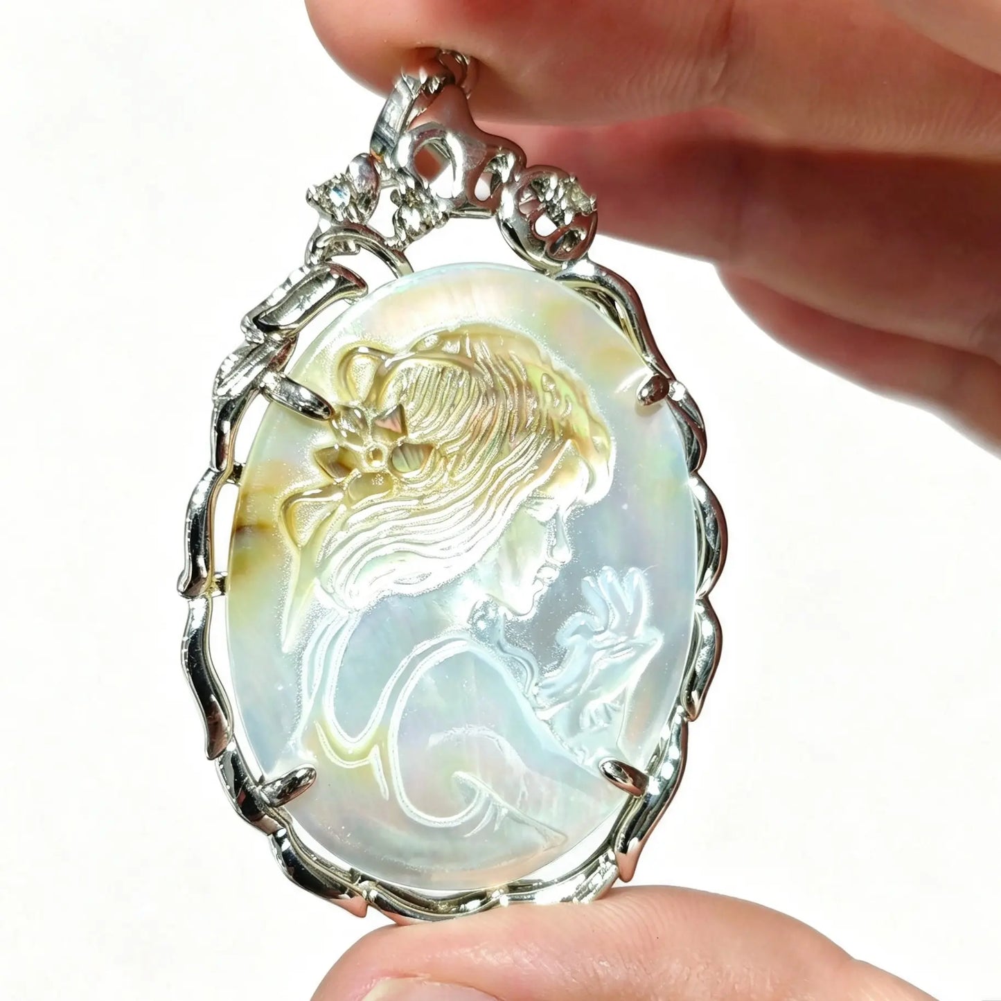 Hand holding a 40mm oval gray mother of pearl cameo pendant featuring carved maiden relief in silver filigree frame