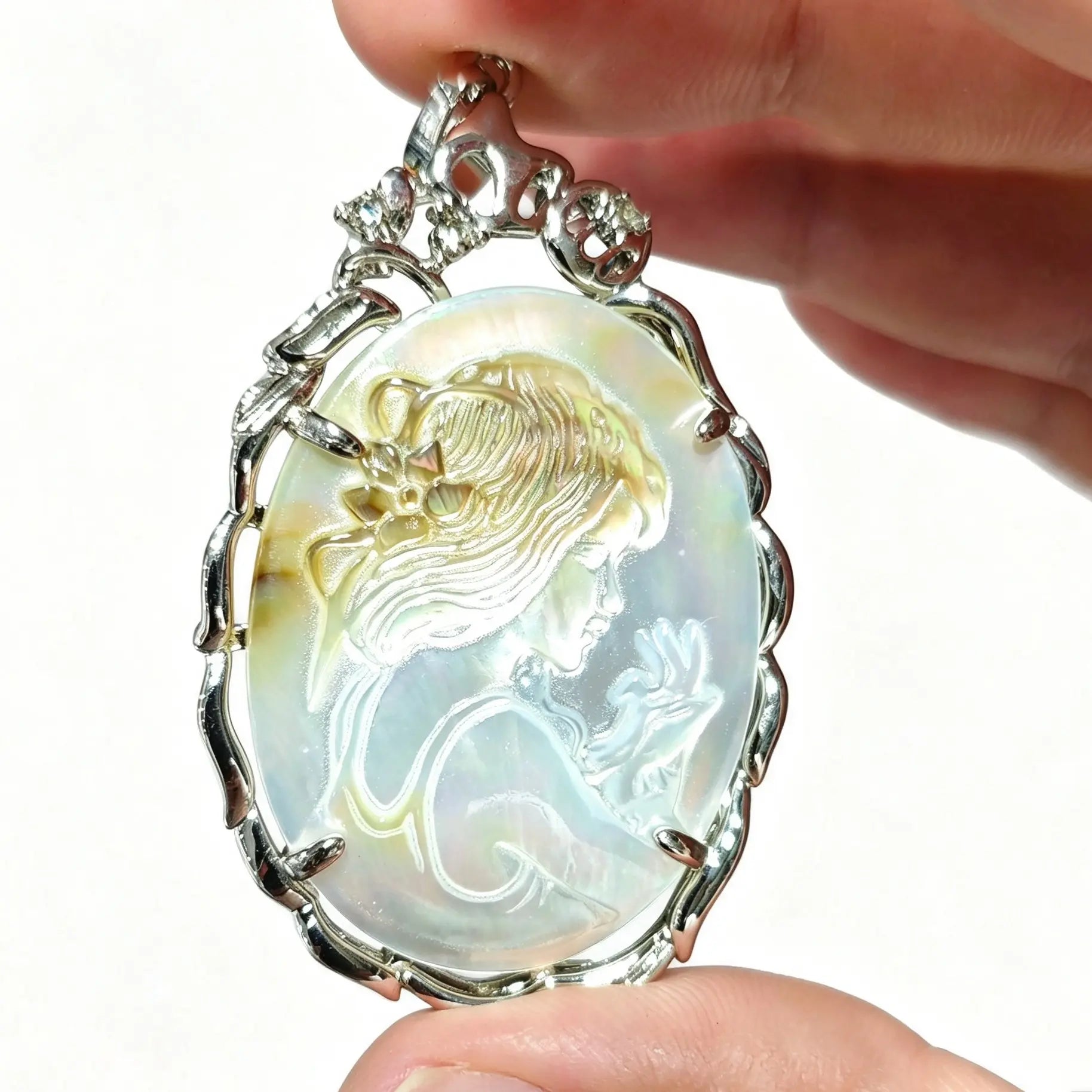 Hand holding a 40mm oval gray mother of pearl cameo pendant featuring carved maiden relief in silver filigree frame