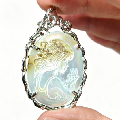 Hand holding a 40mm oval gray mother of pearl cameo pendant featuring carved maiden relief in silver filigree frame