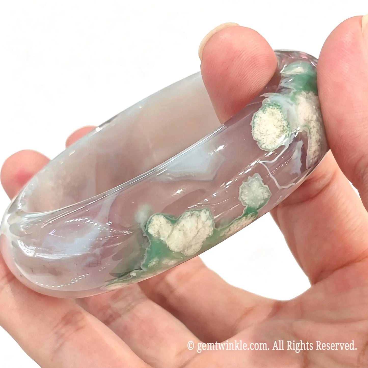 Handheld perspective showing the smooth surface polish and green floral patterns on the cherry blossom agate bangle