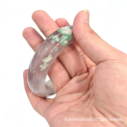 Tilted handheld view of one of a kind green cherry blossom agate bangle held between fingers