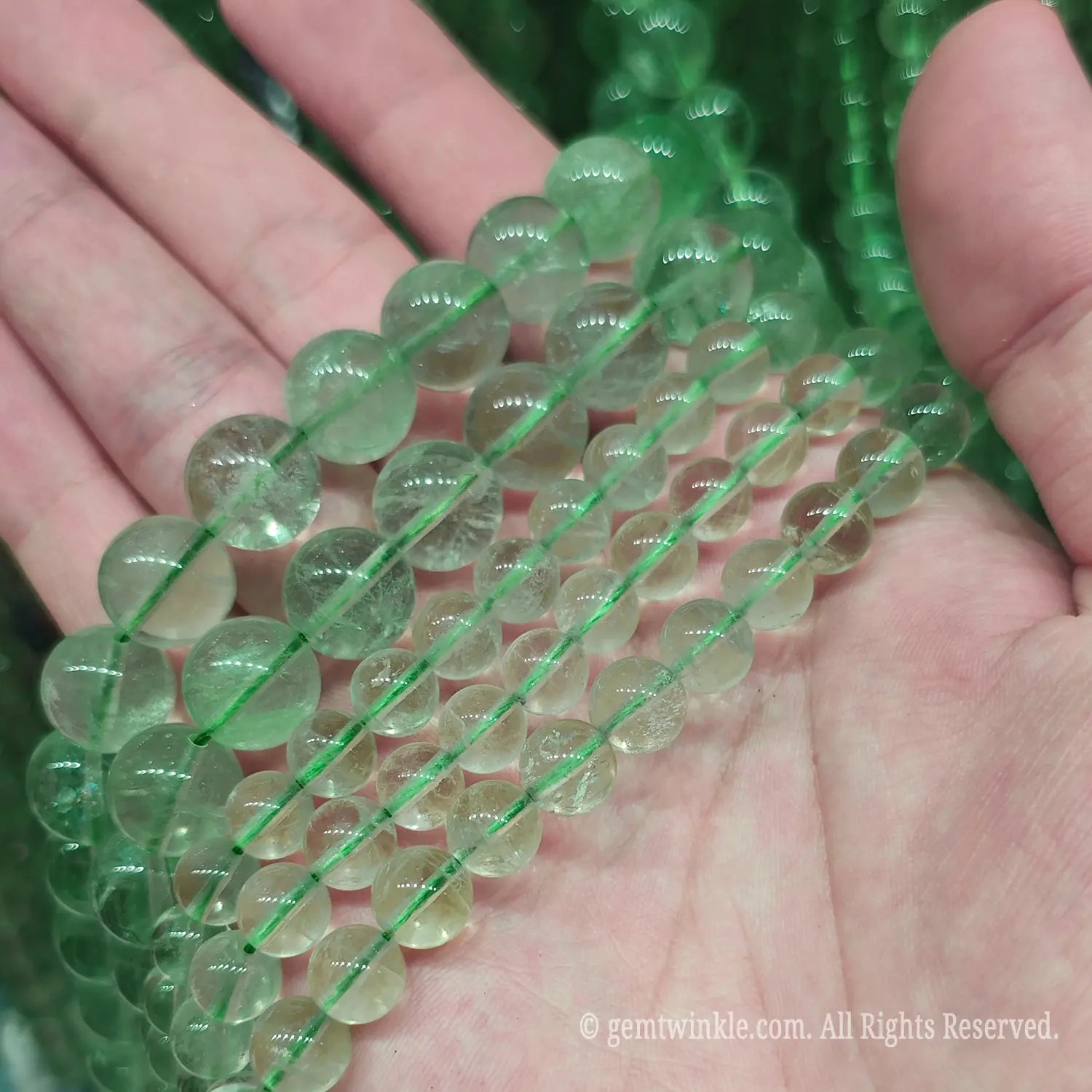 Size comparison of natural green fluorite crystal round beads from 4mm to 14mm held in hand for boutique jewelry creators