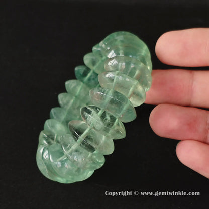 Angle view of natural green fluorite wide statement bangle held under soft studio lighting