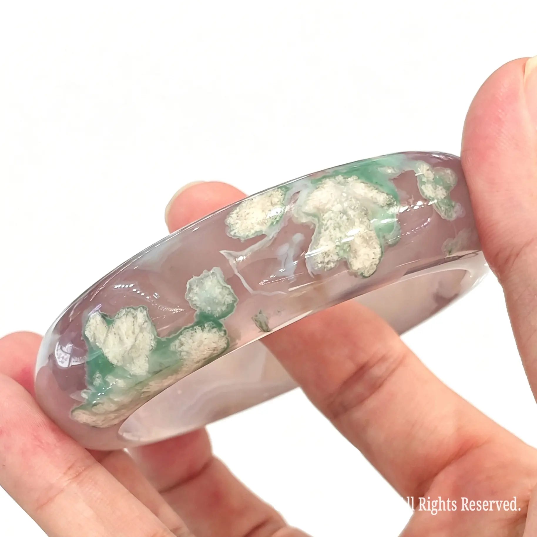 Horizontal view of green cherry blossom agate bangle resting across fingers showing body transparency