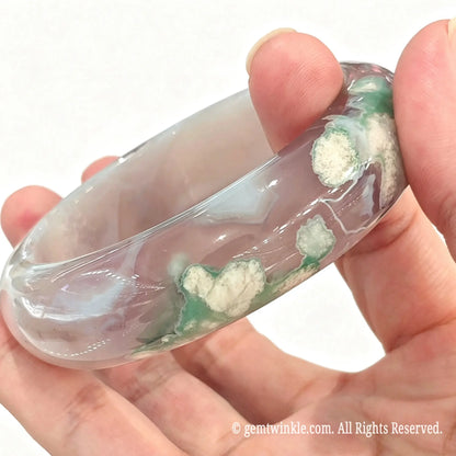 Side angle handheld view of natural green sakura agate bangle displaying outer curvature and green blossom clusters