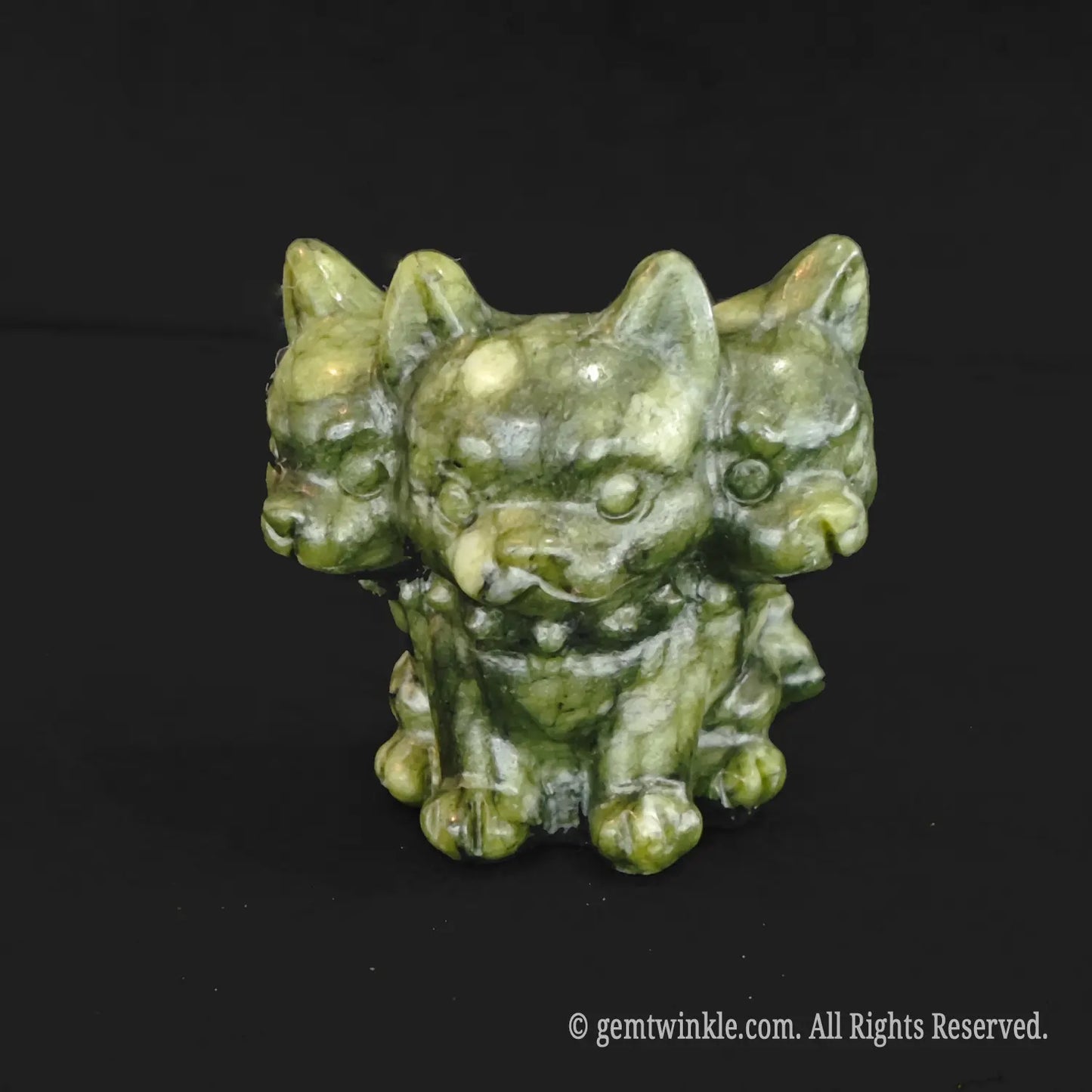 A standalone front view of a dark mottled green serpentine three headed dog figurine showcasing rustic earthy mineral textures and detailed face carvings