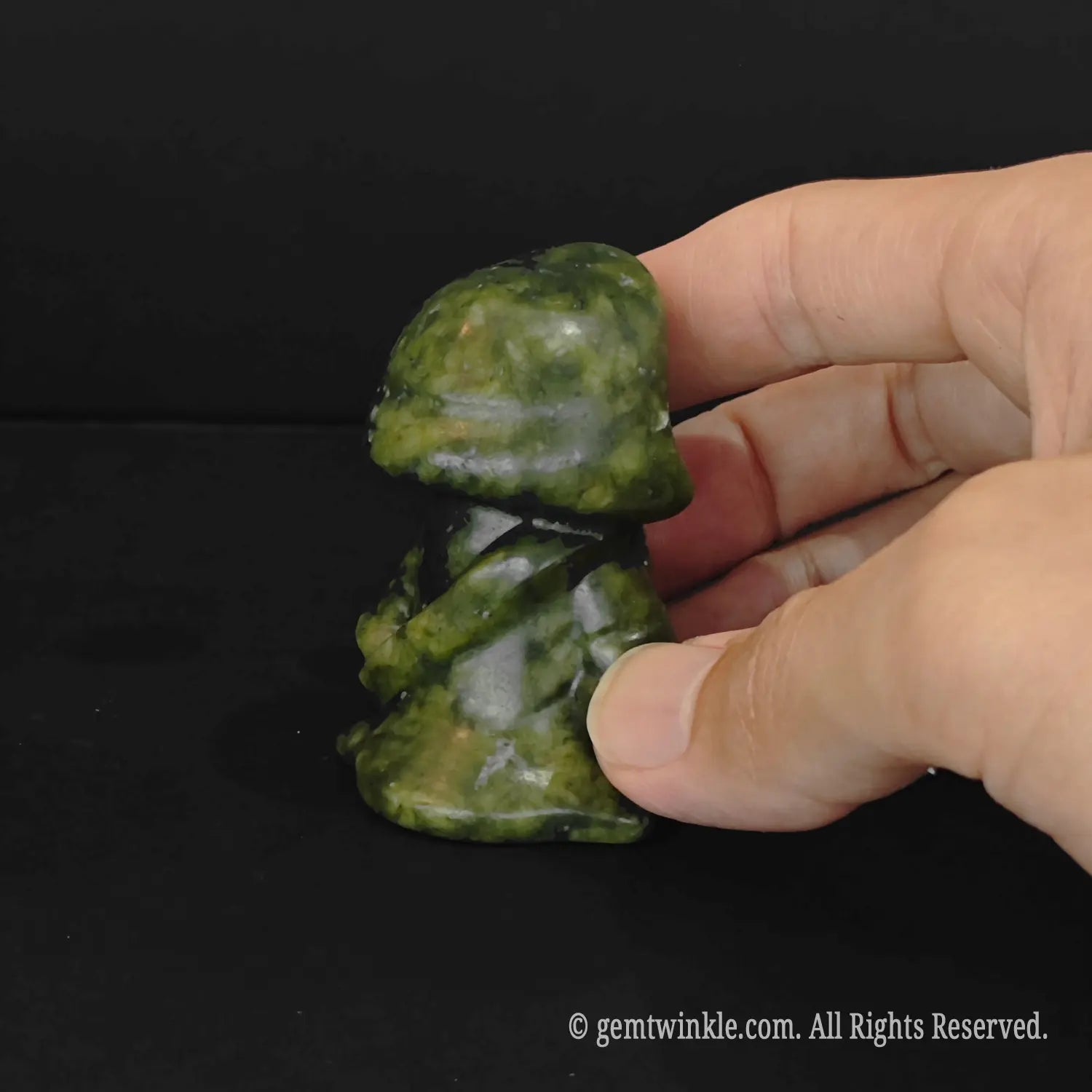 A side profile view of an olive green serpentine grim reaper figurine held by fingers displaying the detailed cloak