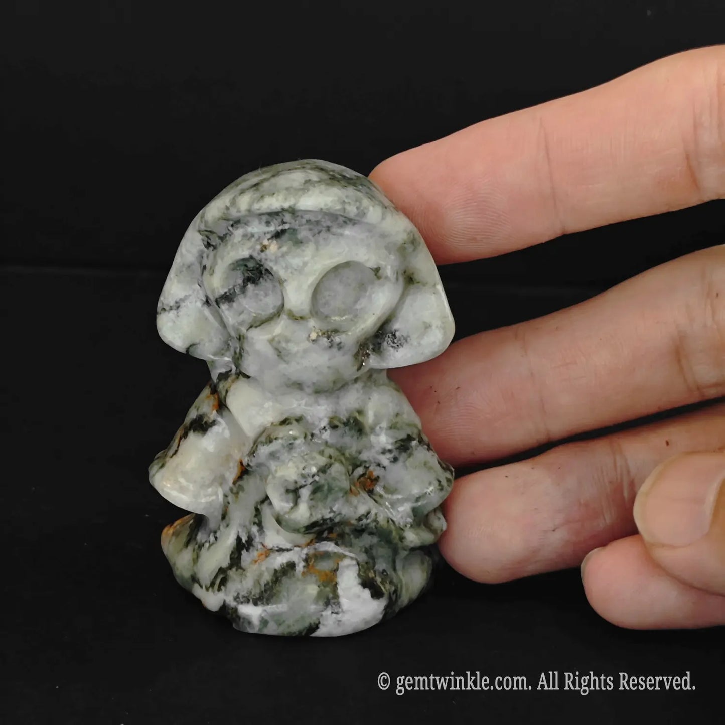 A close up of a hand holding a green spotted stone cute reaper carving showcasing unique speckled mineral patterns