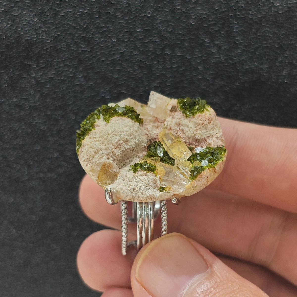 Green epidote quartz crystal cluster ring held in hand side view displaying organic mineral texture