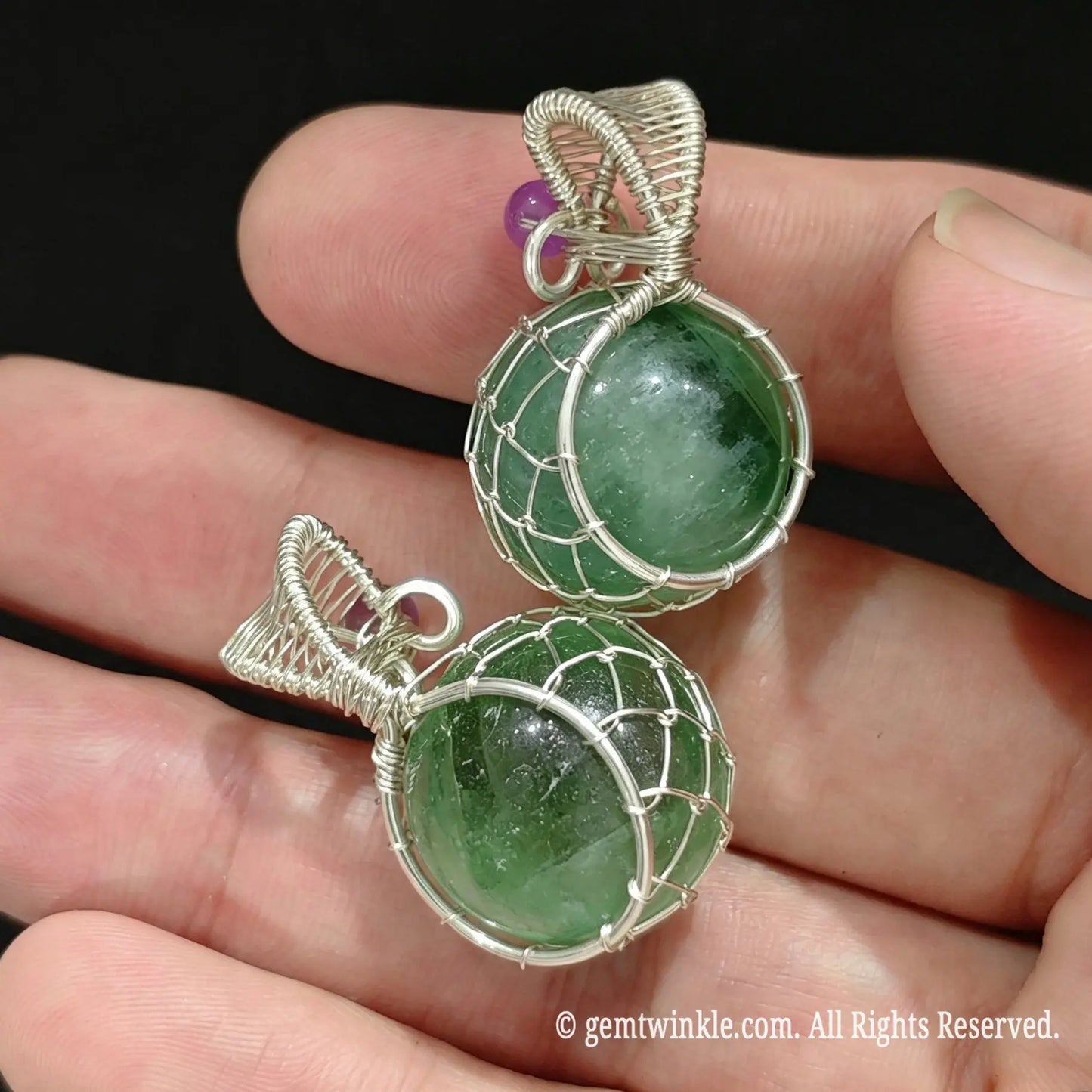 Pair of silver wire wrapped green fluorite sphere pendants resting on palm showing emerald green color