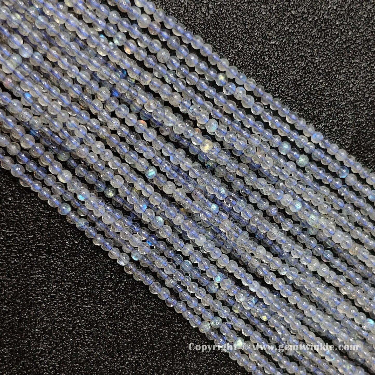 Full view of multiple delicate natural grey blue moonstone round seed strands on dark background