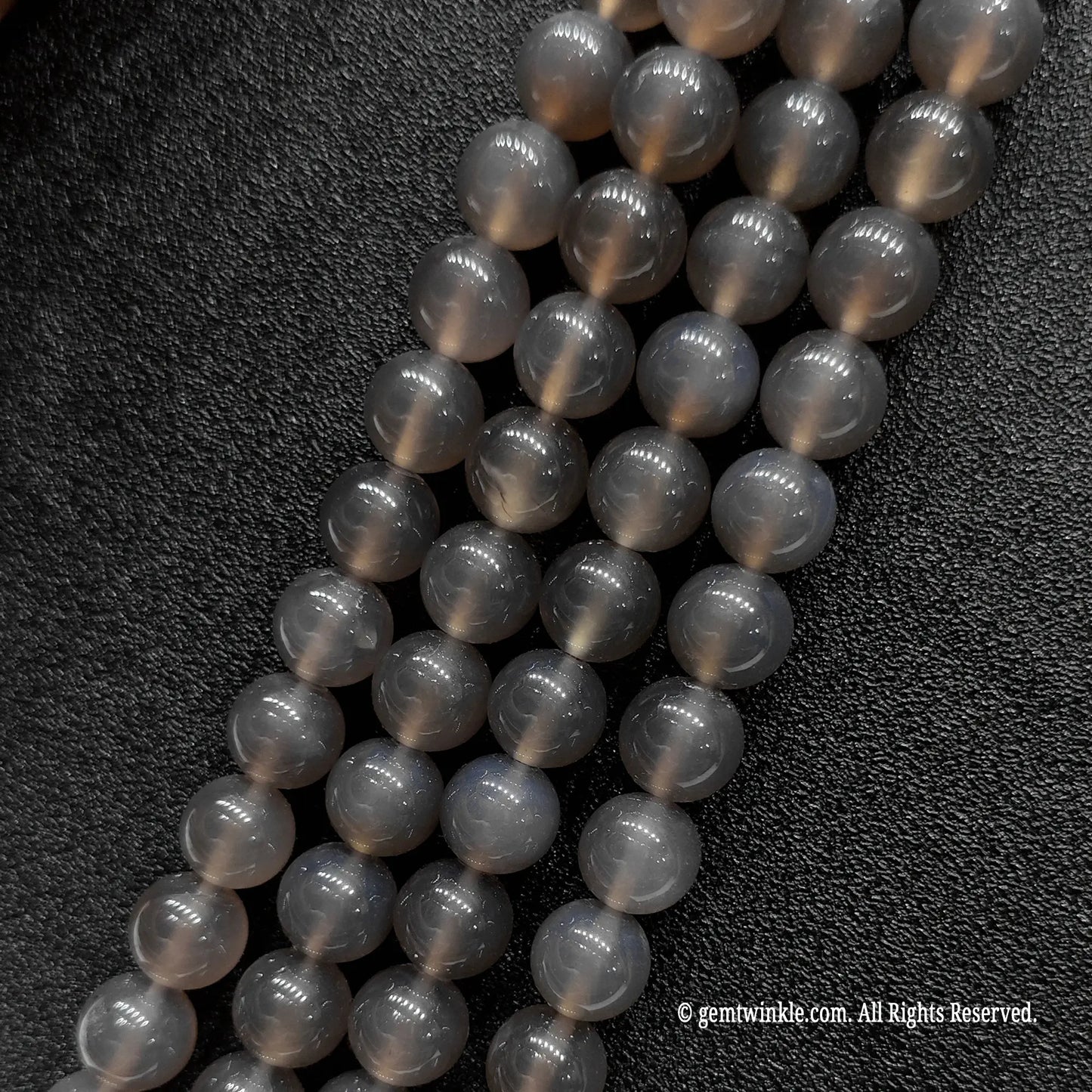 Four parallel bulk strands of polished grey chalcedony mineral loose beads arranged to check batch color consistency