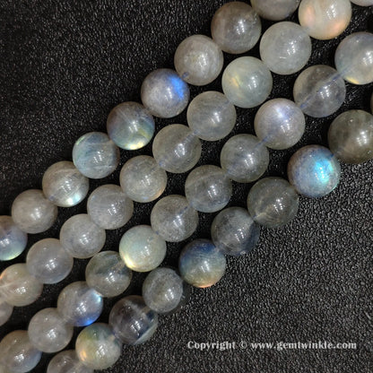 Hand holding natural grey moonstone round bead strands demonstrating bead size scale and optical light play