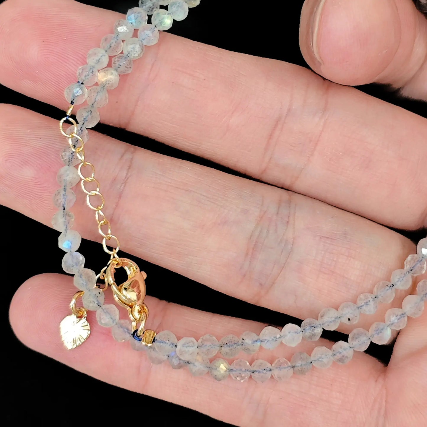 grey moonstone micro faceted bead strand held in hand with gold clasp
