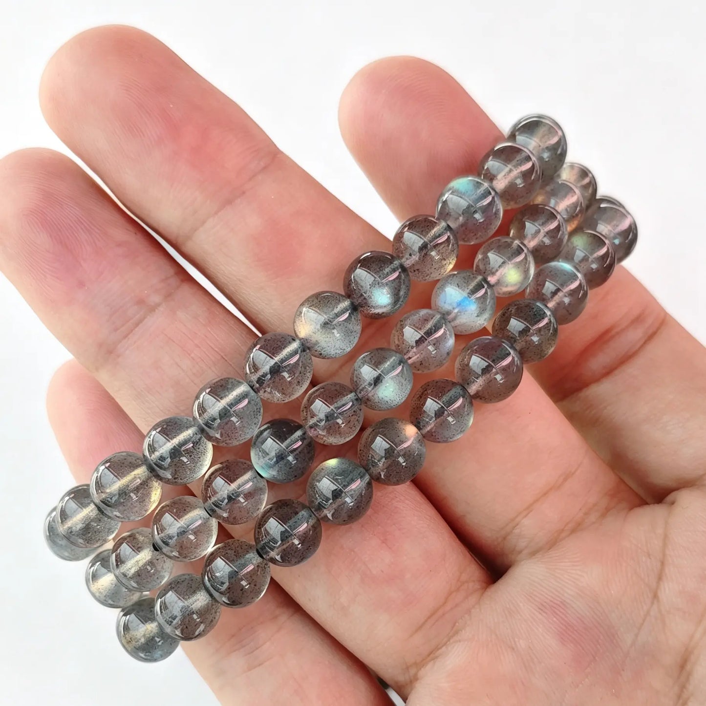 Single-strand grey moonstone round bead bracelet held on fingers showing blue optical flash
