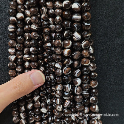 Hand holding natural grey mother of pearl bead strands demonstrating scale for jewelry supply