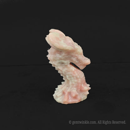 A rare 7cm natural pink opal dragon head carving resting on a dark surface highlighting soft pastel pink textures