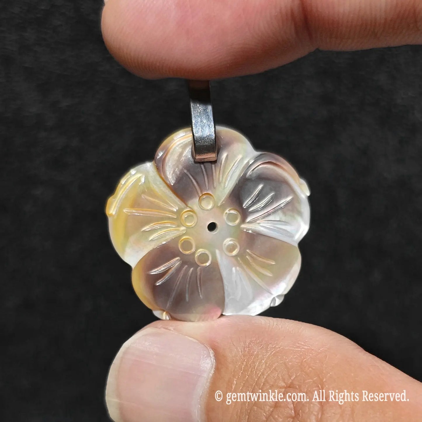 Mini precision carved grey mother of pearl blossom pendant displayed on fingertips for accurate 25mm size reference