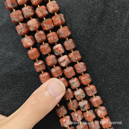 Artisan fingers holding red sesame jasper strands to demonstrate bead scale and texture