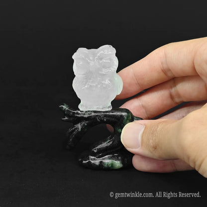 Hand holding a 3 inch white quartz owl figurine on a green stone branch to show actual size
