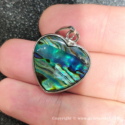 Handheld perspective showing 25mm heart abalone shell pendant with bright blue green iridescence