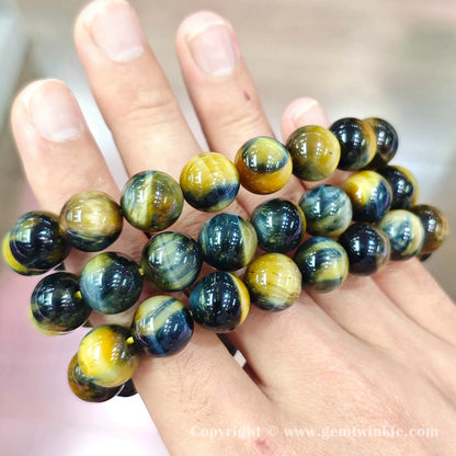 Handheld perspective displaying multiple single strand blue and yellow tiger eye bracelets