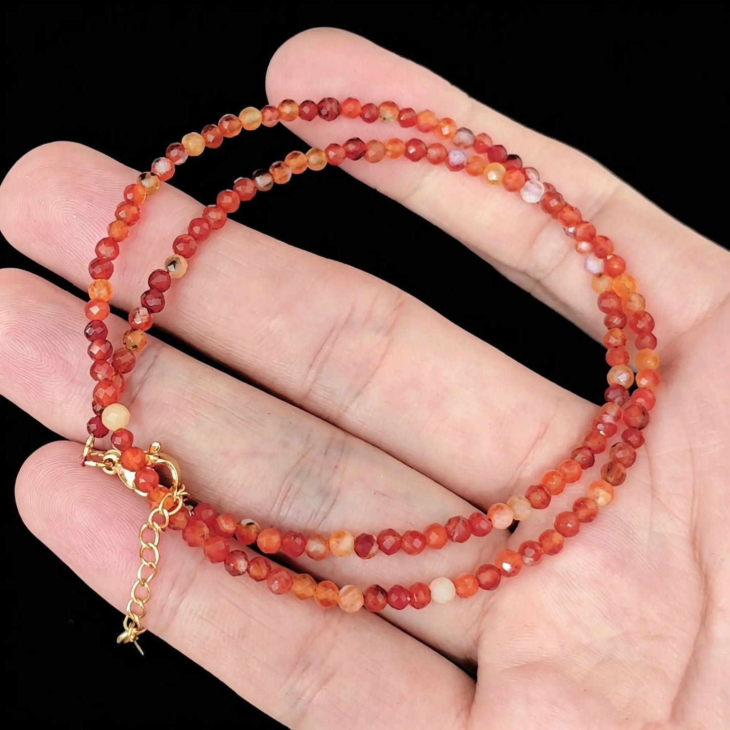 heat treated red banded agate micro faceted bead strand held in hand displaying warm crimson color