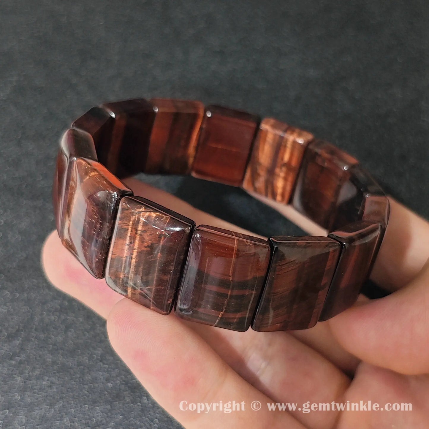 red tigers eye plate stretch bracelet held over open palm displaying silky chatoyant red bands