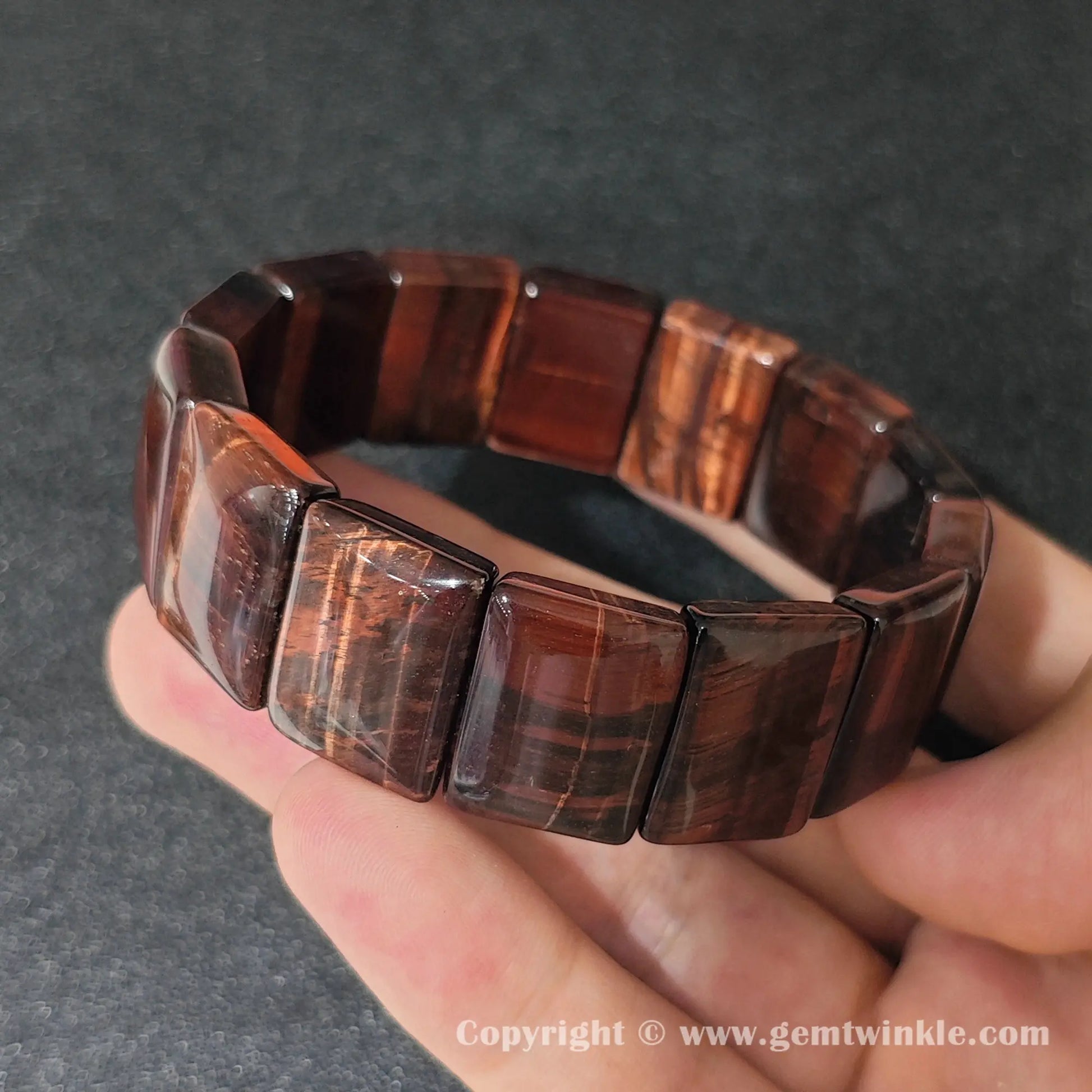 red tigers eye plate stretch bracelet held over open palm displaying silky chatoyant red bands
